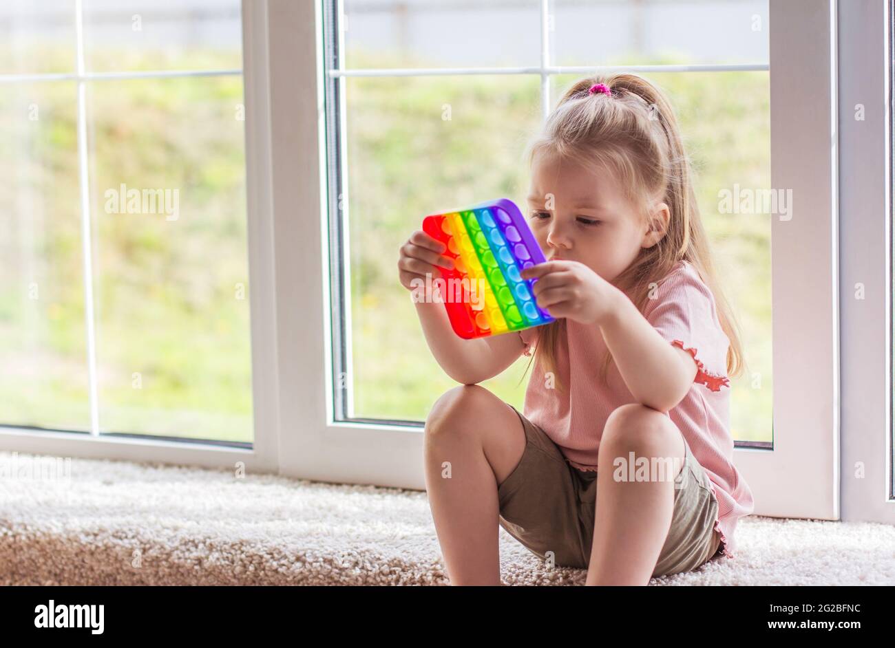 I bambini della bambina bionda giocano con il nuovo giocattolo sensoriale di tendenza - arcobaleno pop esso. Giocattolo antistress per bambini e adult.colorful giocattolo semplice concavità. Squis Foto Stock