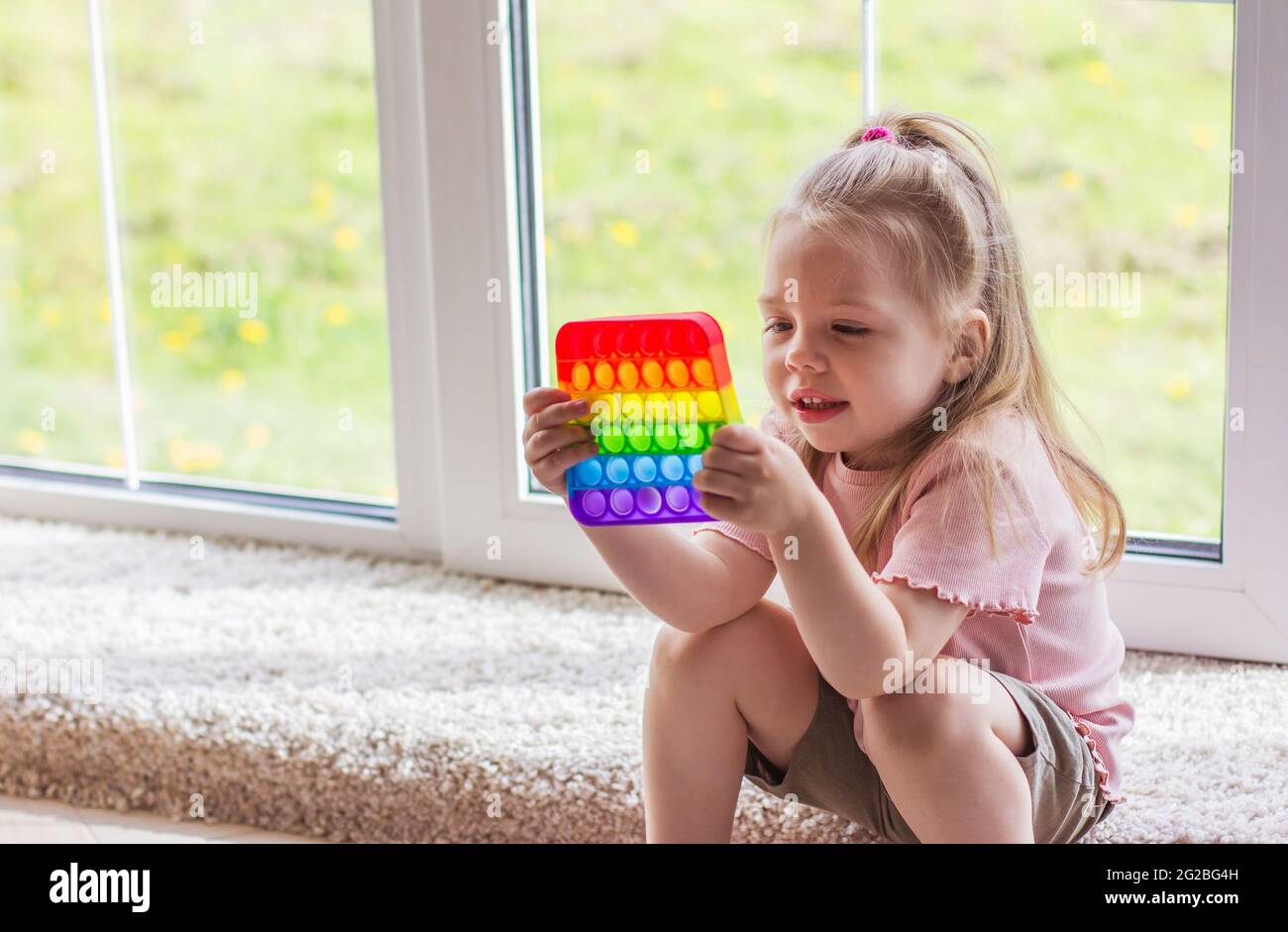I bambini della bambina bionda giocano con il nuovo giocattolo sensoriale di tendenza - arcobaleno pop esso. Giocattolo antistress per bambini e adult.colorful giocattolo semplice concavità. Squis Foto Stock