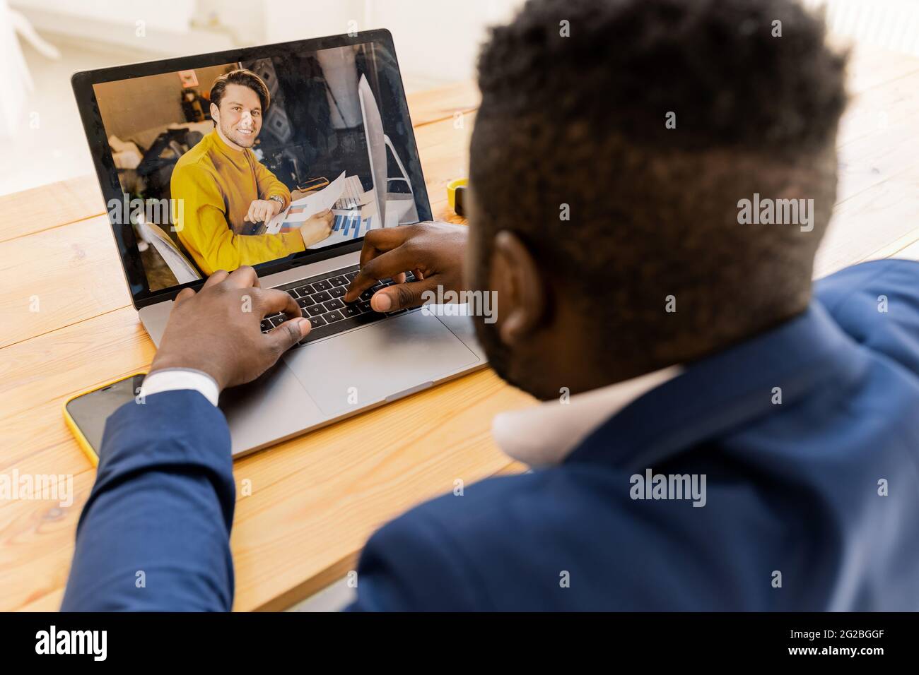 Indietro view Afro American business man digitando sul computer portatile giallo su scrivania, telefono cellulare e tablet, tenere una riunione online, pianificare un nuovo progetto Foto Stock