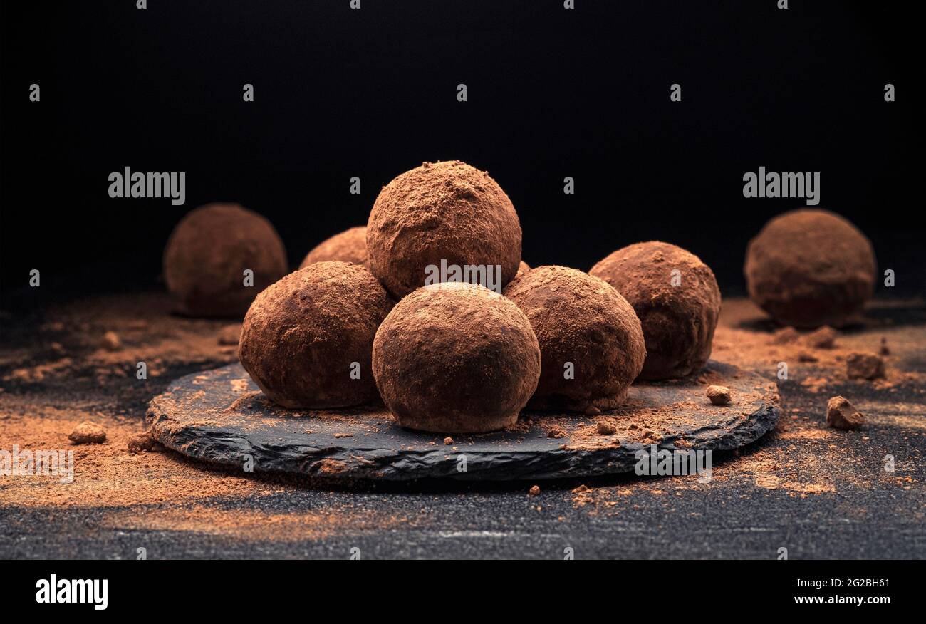Tartufi di cioccolato, caramelle di cioccolato rotonde su sfondo di ardesia nera con polvere di cacao Foto Stock