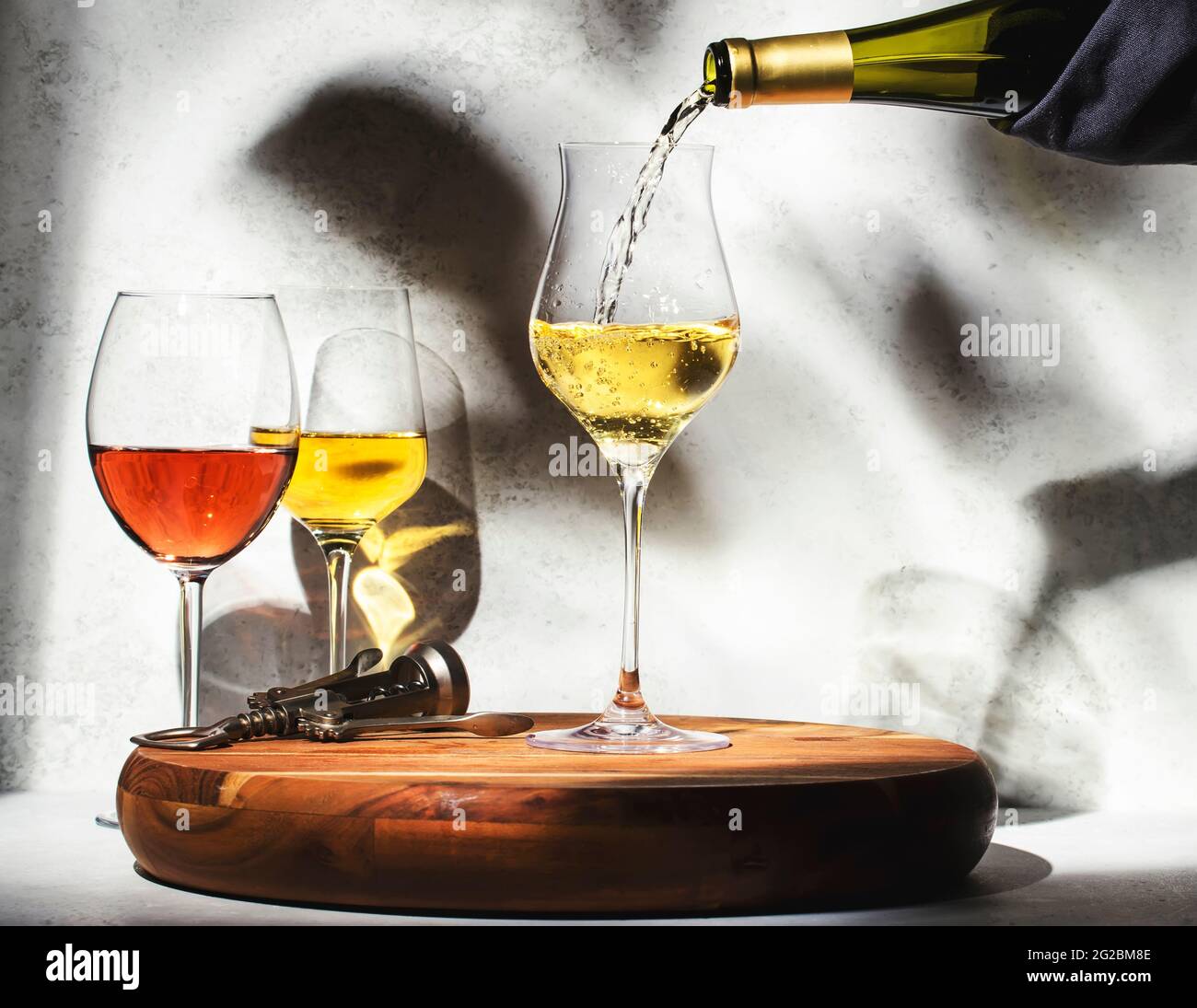 Degustazione di vini. Vino bianco in calice su sfondo con selezione di vini rossi, bianchi e rosati in calici. Luce solare e ombre dalla folia Foto Stock