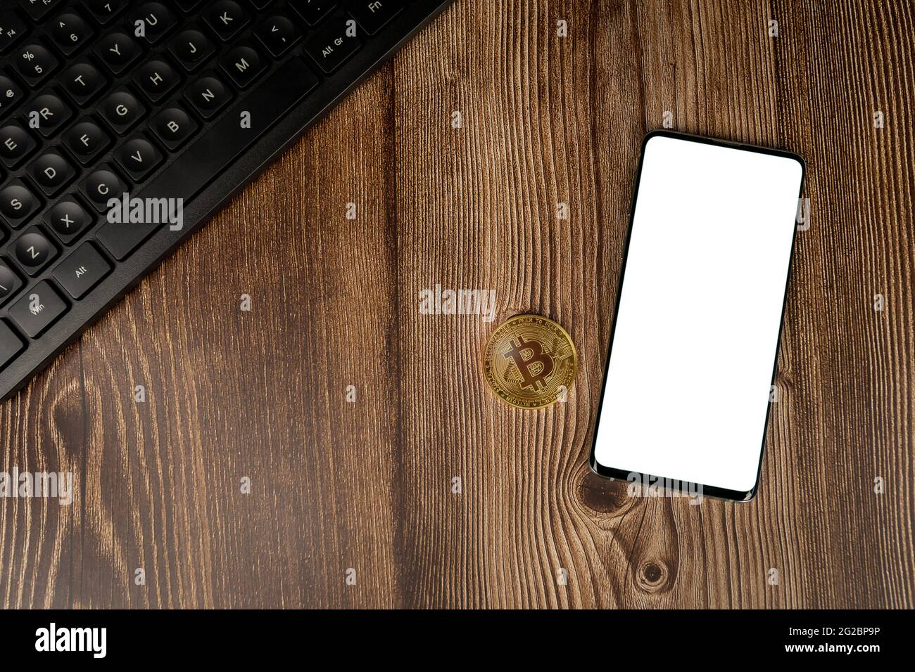 Smartphone con mockup bianco sullo schermo e moneta bitcoin criptovaluta con tastiera nera su sfondo in legno con spazio per la copia. Modello Foto Stock