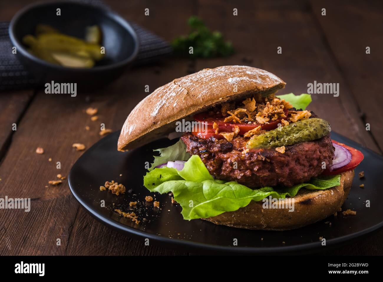 Hamburger con polpettine vegetariano di hamburger, insalata, pomodori e cipolle arrostite su un piatto nero su un tavolo di legno Foto Stock