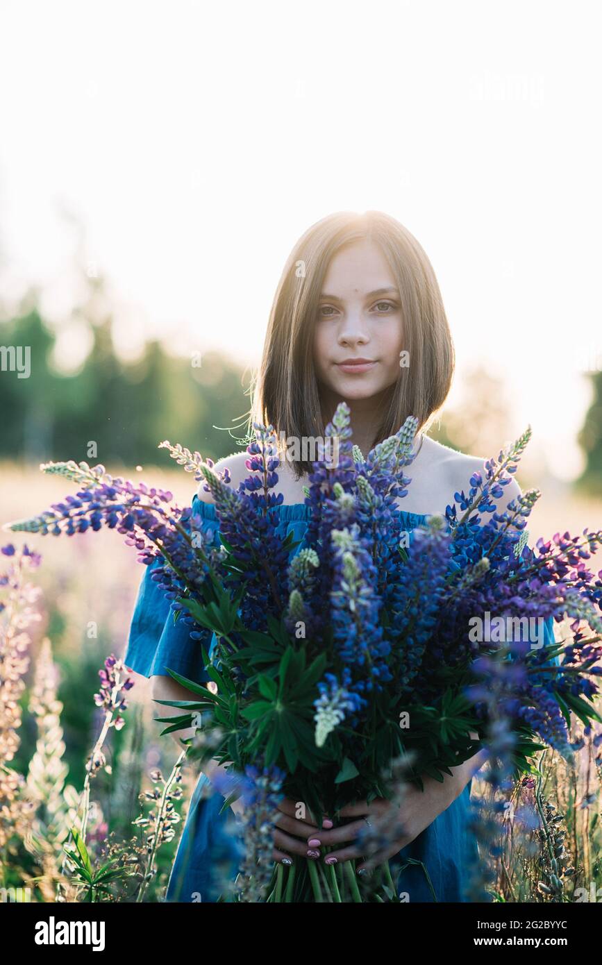 Giovane bella donna in un vestito si trova in un campo di lupini. La ragazza tiene un grande bouquet di lupini viola in un campo fiorito. Fiore lupino in fiore Foto Stock