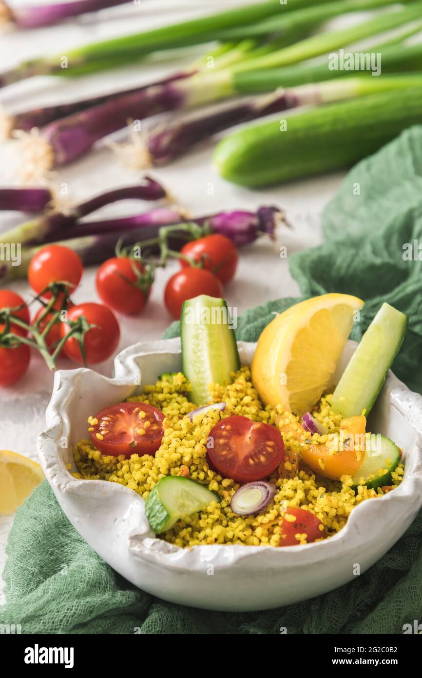 Insalata couscous con cetriolo, pomodori e cipolle in una ciotola bianca, verdure colorate, verticale Foto Stock