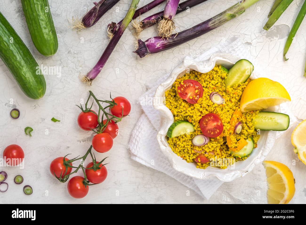 Insalata couscous sana con cetrioli, pomodori e cipolle in una ciotola bianca su sfondo bianco, decorata con verdure colorate, vista dall'alto Foto Stock