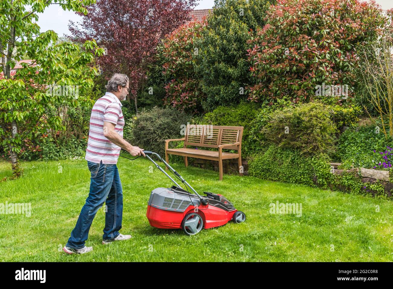 Uomo che taglia il prato nel suo giardino Foto Stock