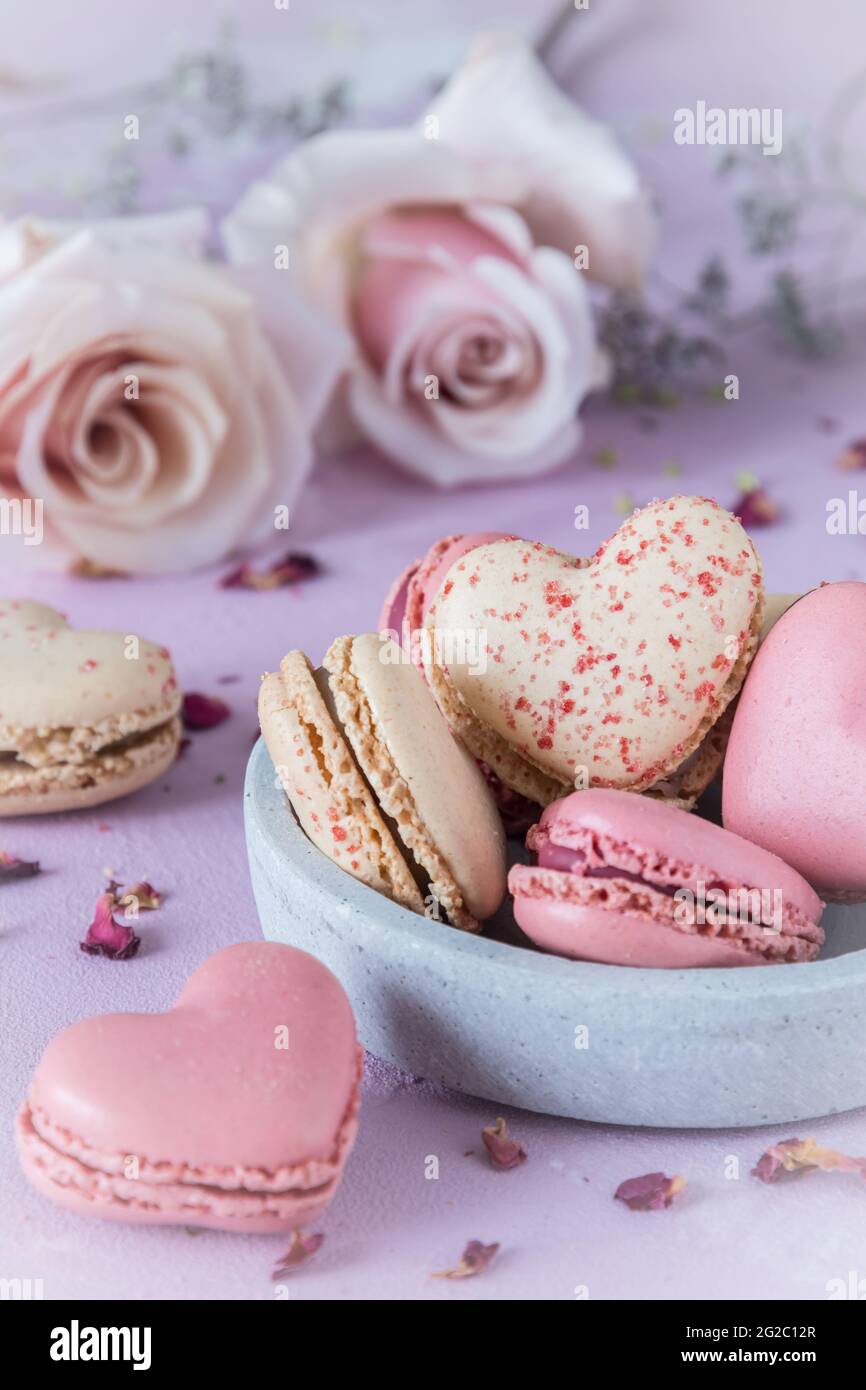 Macaroni dolci a forma di cuore e rose in colori pastello su una base rosa. Un delizioso dessert o un regalo per San Valentino o la Festa della mamma. Verticale. Foto Stock