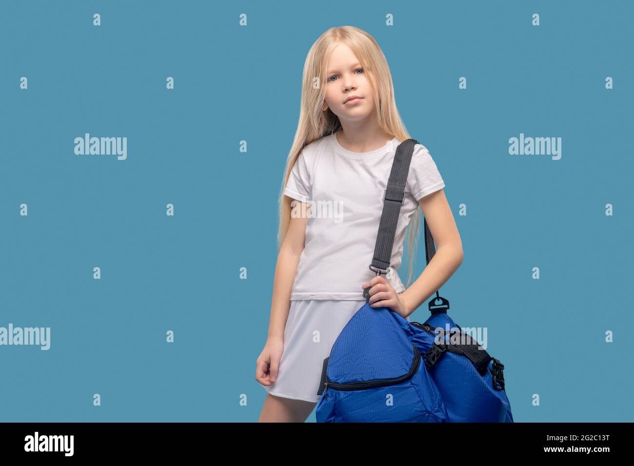 Ragazza con borsa sportiva in piedi su sfondo blu Foto Stock