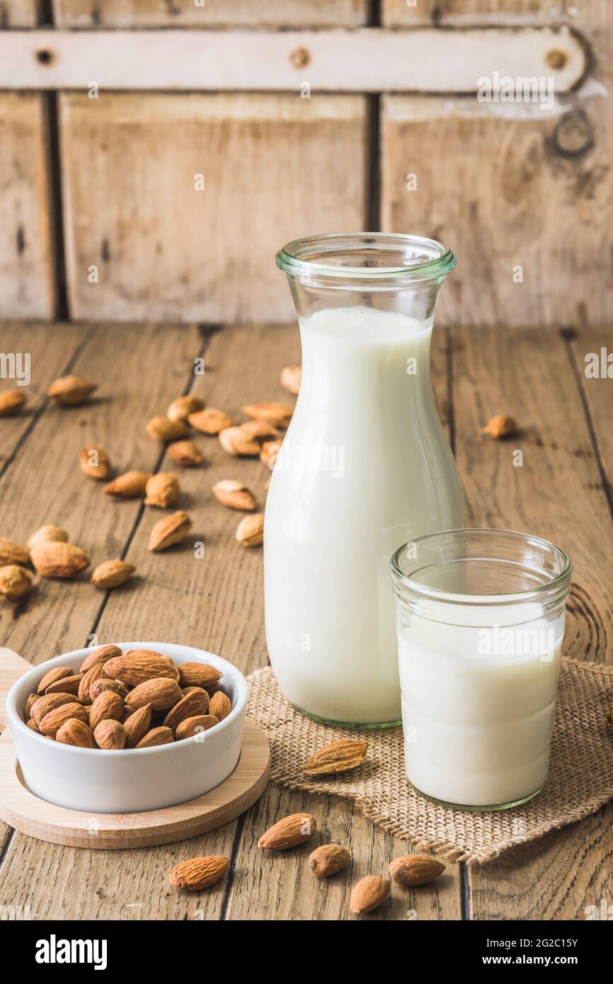 Bicchiere e caraffa con latte di mandorle vegane, noccioli di mandorle e mandorle intere su un vecchio tavolo rustico in legno, verticale Foto Stock