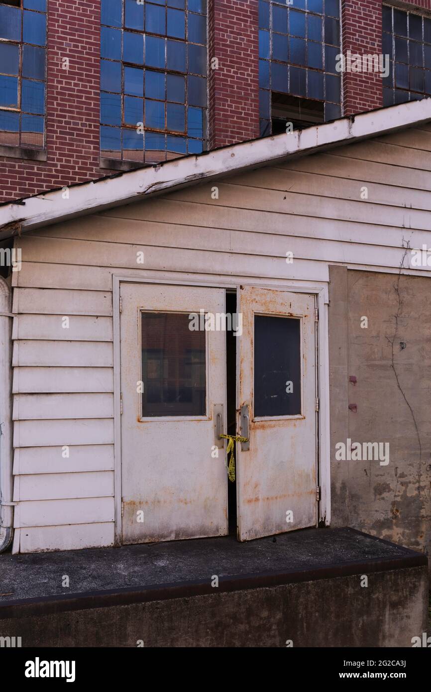 ELKIN, NC, USA-5 GIUGNO 2021: Porte doppie in un vecchio edificio di stoccaggio abbandonato con un piccolo molo di carico in un sito industriale. Immagine verticale. Foto Stock