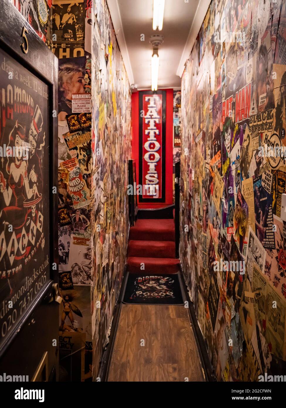 Tatuaggio Parlour. L'entrata a porta aperta e il corridoio decorato a poster ad un salotto tatuaggio nelle strade secondarie di Soho, nel centro di Londra. Foto Stock