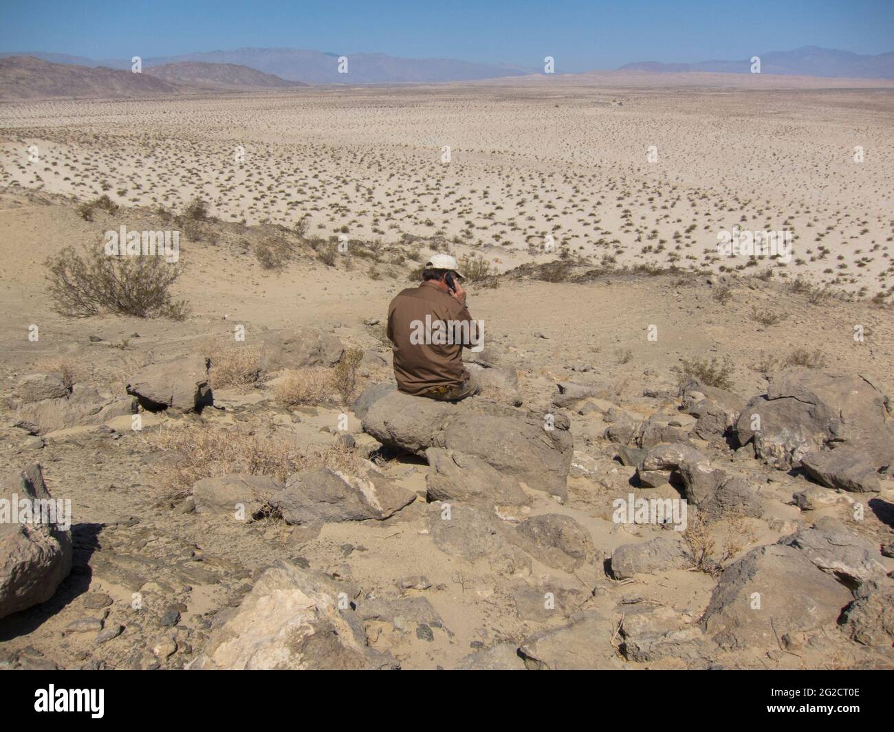 Un uomo seduto sulle rocce, facendo una chiamata del telefono cellulare nel mezzo del deserto. A Borego Springs, California. Foto Stock