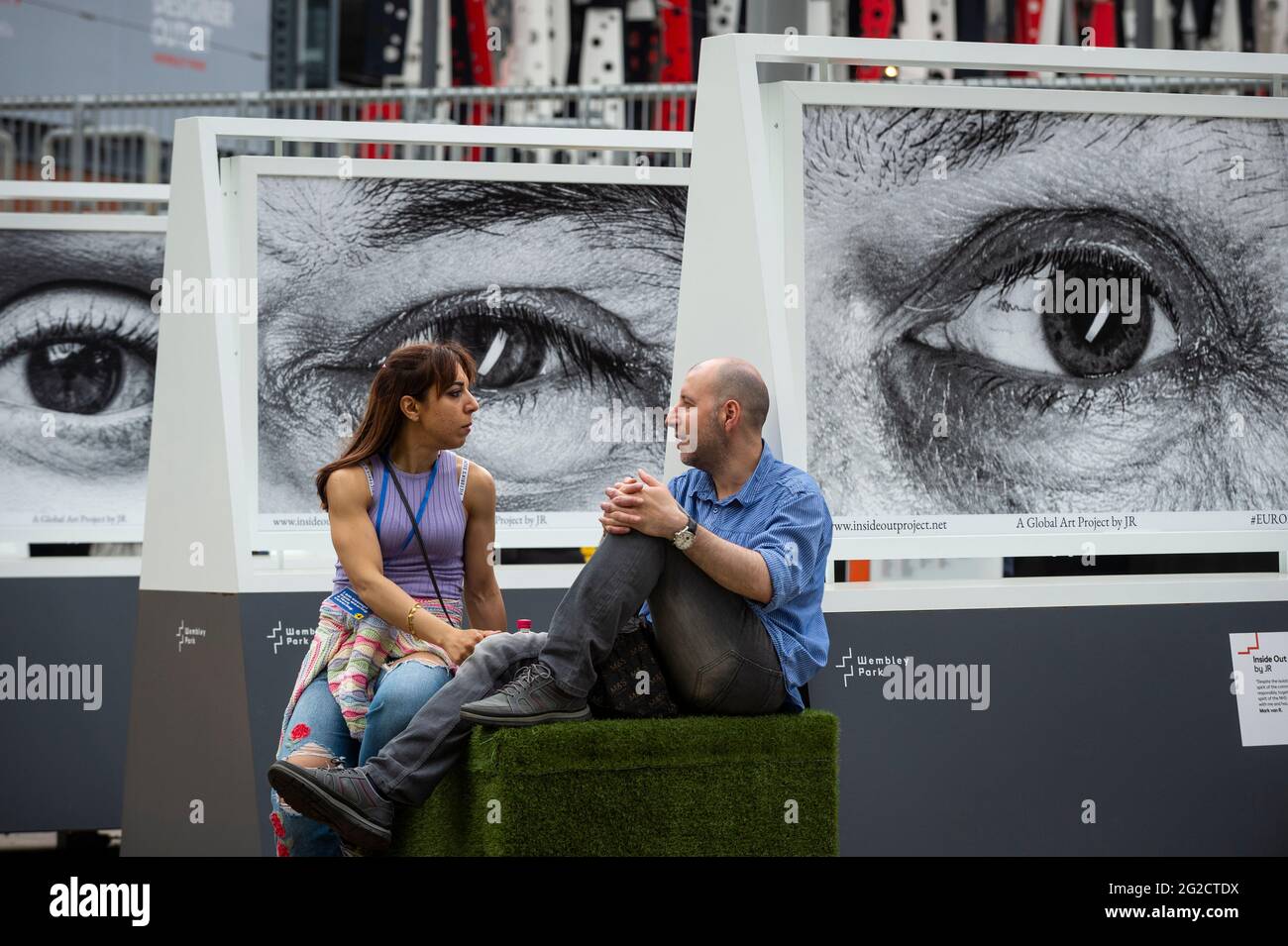 Londra, Regno Unito. 10 giugno 2021. Una coppia si siede di fronte a un'installazione di opere dell'artista francese JR per il progetto Inside out Outside Wembley Stadium prima dell'inizio di Euro 2020. Molti dei soggetti nei lavori sono lavoratori della NHS durante la pandemia di coronavirus in corso. Credit: Stephen Chung / Alamy Live News Foto Stock