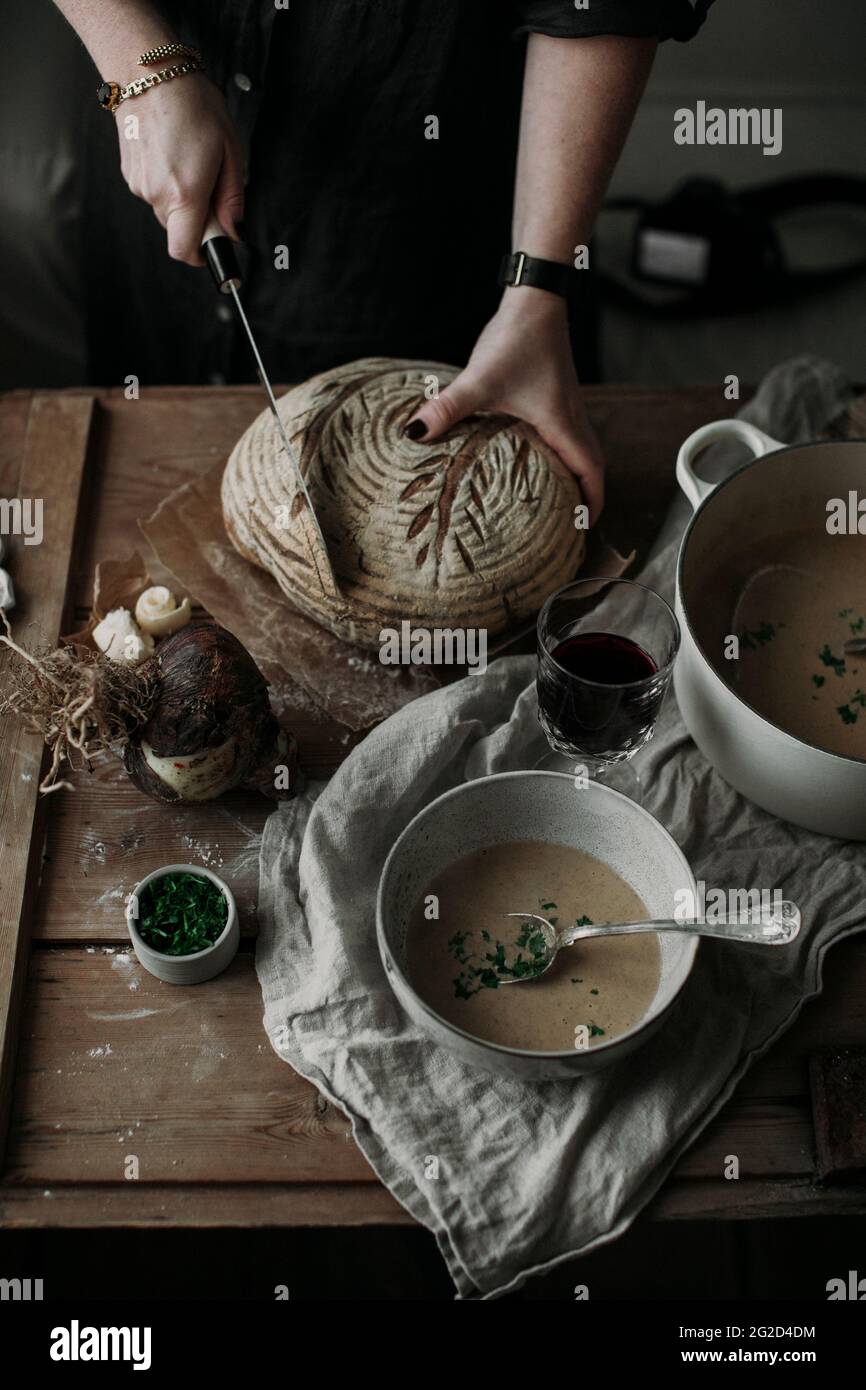 Donna che taglia il pane fatto in casa accanto alla ciotola della zuppa Foto Stock