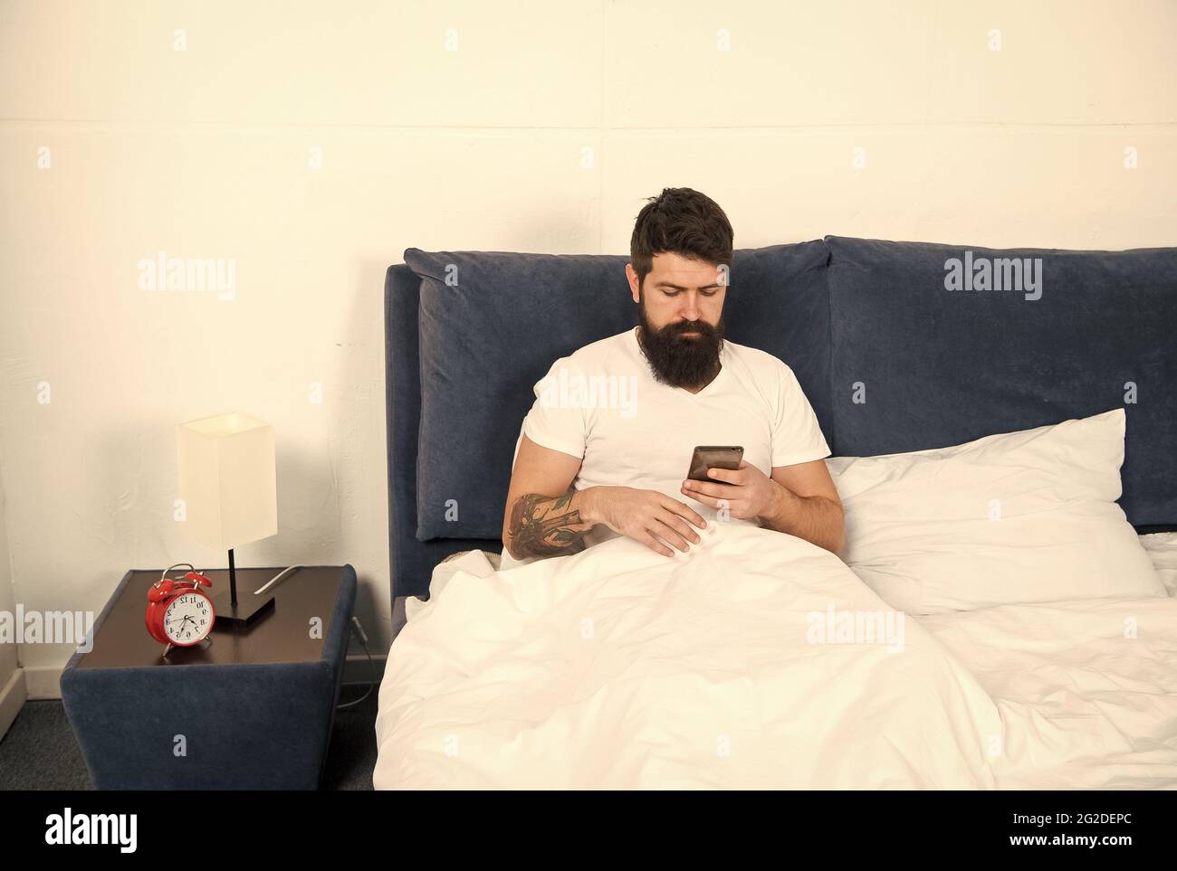 Andare online. L'uomo con la bearded usa lo smartphone a letto. Tecnologia per la casa. Adozione della tecnologia mobile. Tecnologia a banda larga. Nuova tecnologia. Vita moderna Foto Stock