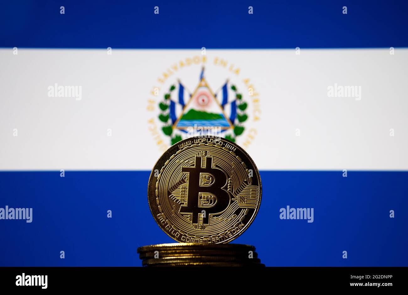 Moneta di rappresentanza Bitcoin posta di fronte alla bandiera nazionale offuscata di Salvador. El Salvador è il primo paese ad adottare il bitcoin come valuta legale. Co Foto Stock