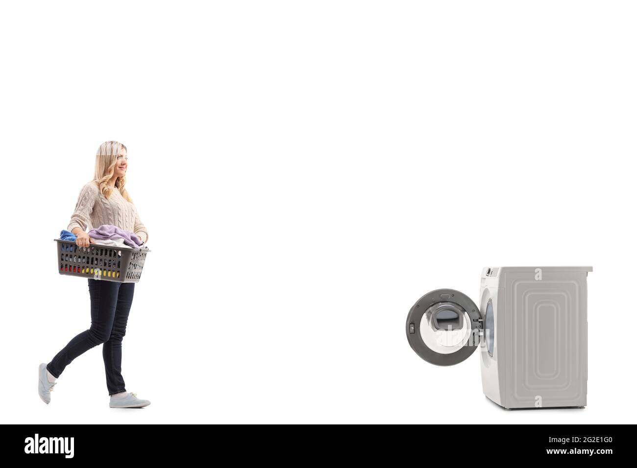 Foto di profilo a lunghezza intera di una donna con un cesto di biancheria pieno di vestiti e camminando verso una lavatrice isolata su sfondo bianco Foto Stock