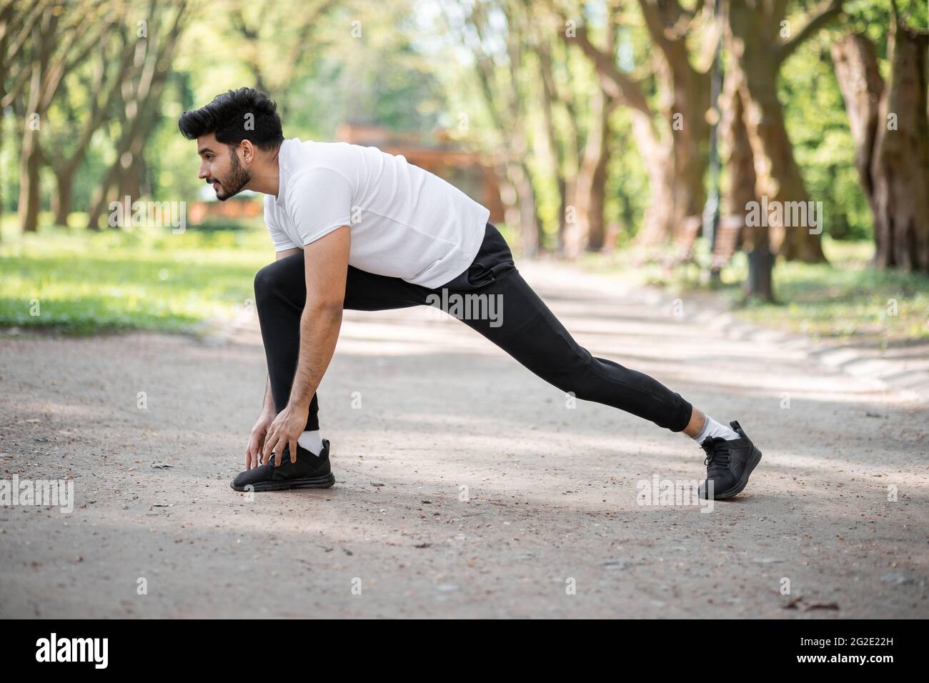 Giovane uomo sportivo vestito con abiti sportivi facendo esercizi per  stretching corpo all'aria fresca. Piacevole ragazzo indù che si prepara per  la corsa al verde parco estivo Foto stock - Alamy