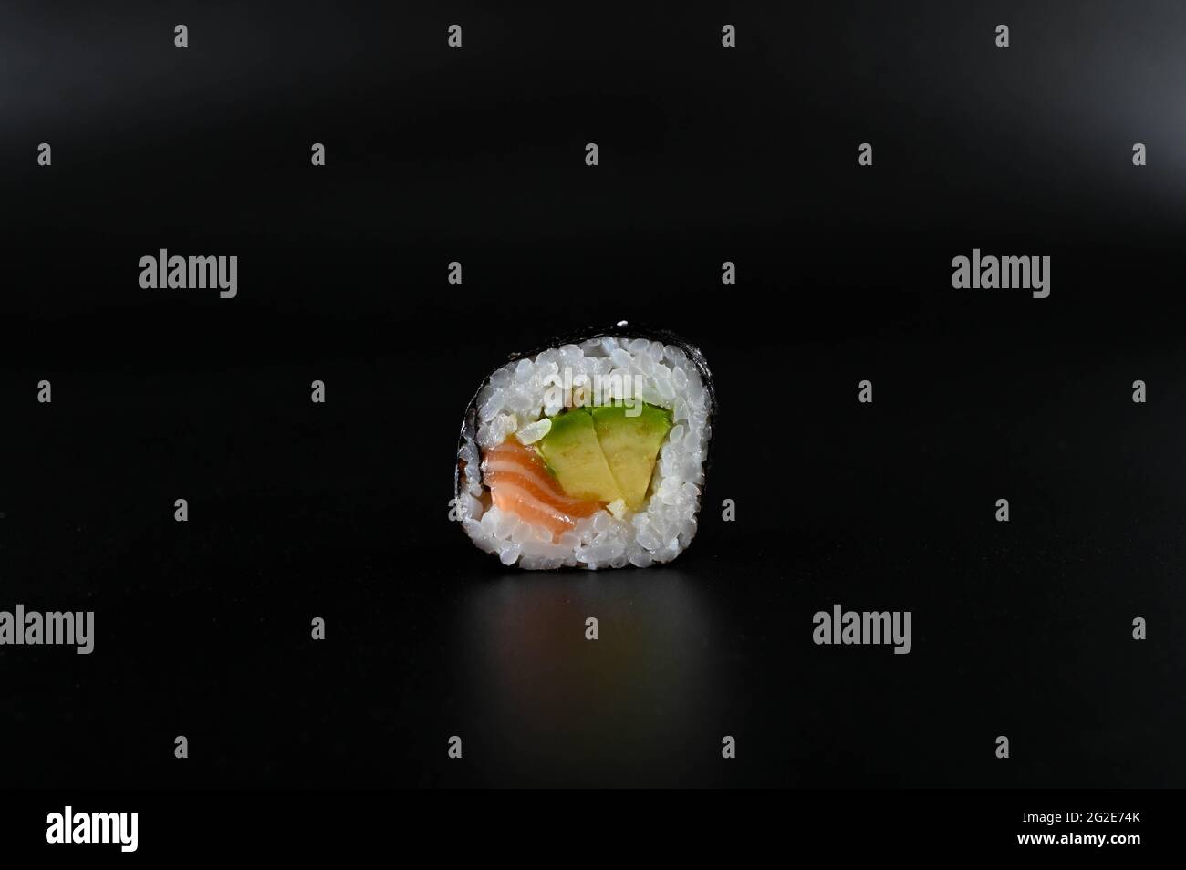 Primo piano di un pezzo di sushi con salmone e avocado su uno sfondo nero isolato. Foto Stock