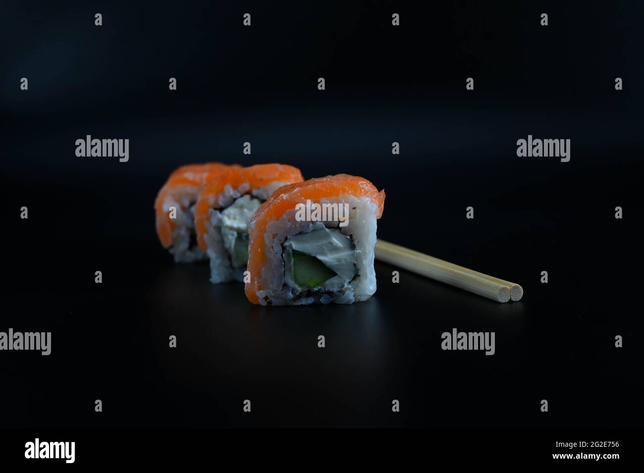 Primo piano di tre pezzi disposti diagonalmente di sushi con bacchette su uno sfondo nero isolato. Foto Stock