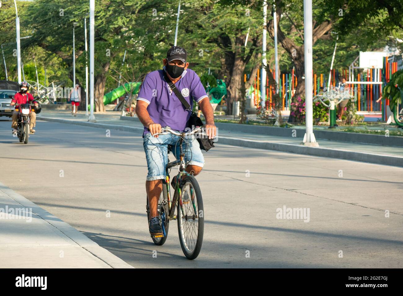 Santa Marta, Magdalena, Colombia - 22 2021 maggio: L'uomo latino che usa una maschera nera e un cappuccio è in bicicletta al mattino in Avenue Park Foto Stock