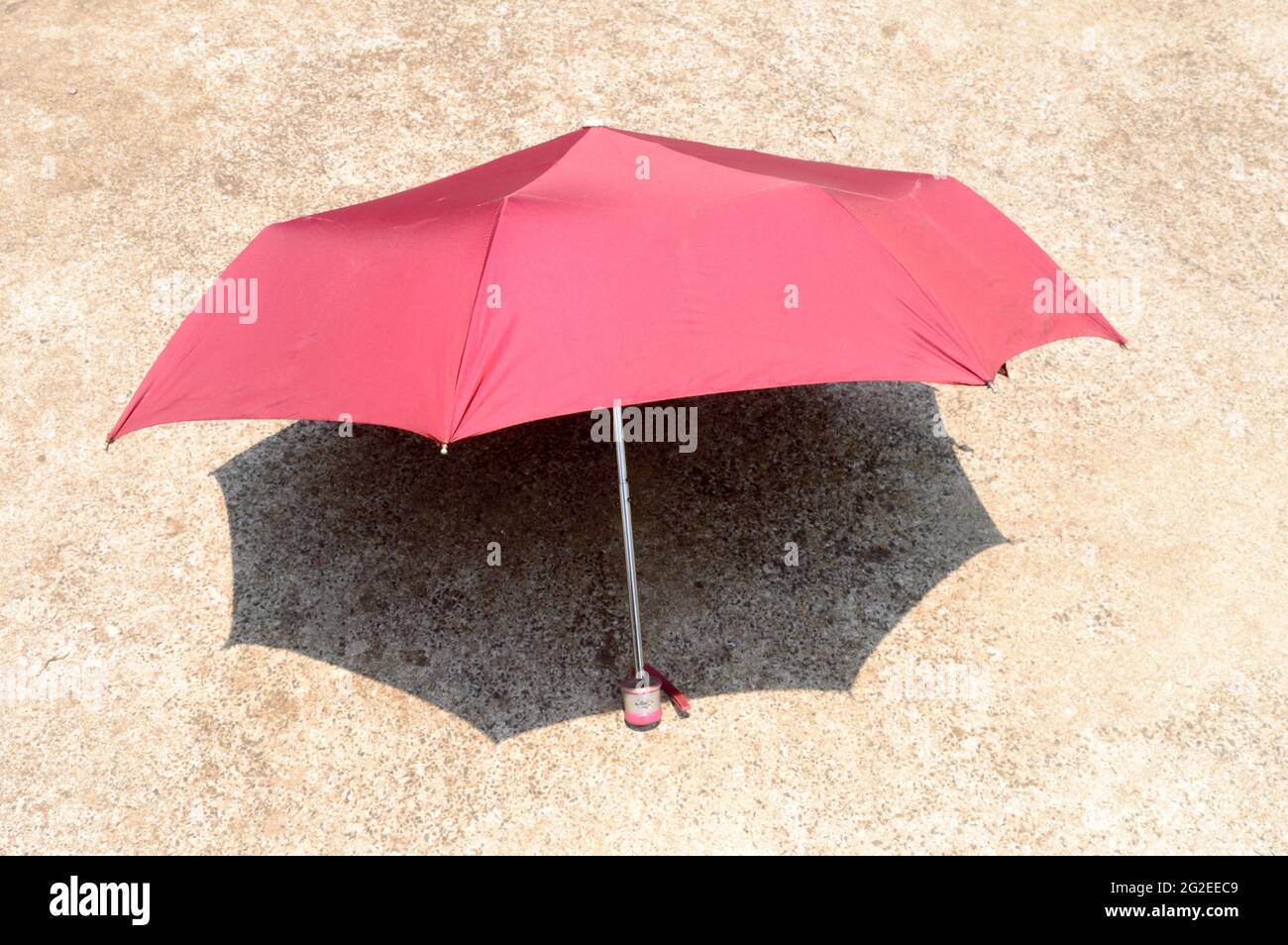 Ombrellone UV al sole estivo. Ombrellone di colore rosso che blocca la luce solare. Ombra sul pavimento sabbioso. Solarium ombra ombra ombra sfondo ombra. Foto Stock