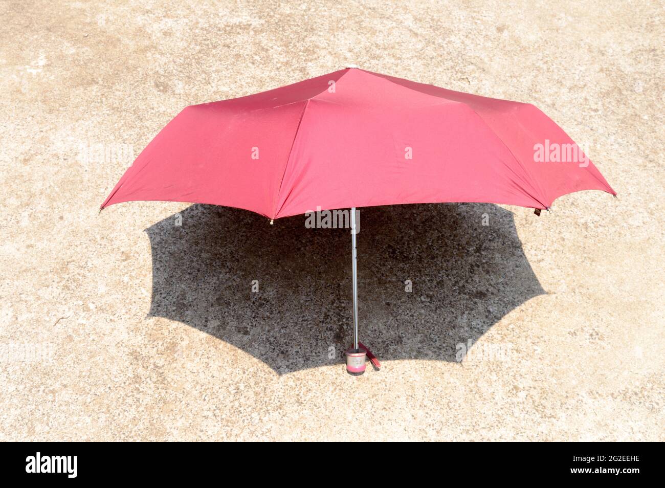 Ombrellone UV al sole estivo. Ombrellone di colore rosso che blocca la luce solare. Ombra sul pavimento sabbioso. Solarium ombra ombra ombra sfondo ombra. Foto Stock