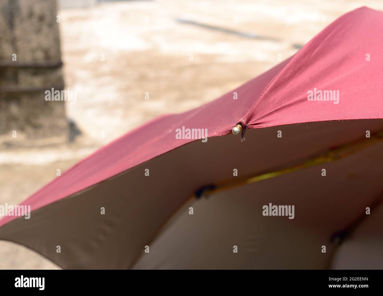 Extreme primo piano di ombrello UV nel sole estivo. Ombrellone di colore rosso che blocca la luce solare. Solarium ombra ombra ombra sfondo ombra. Foto Stock