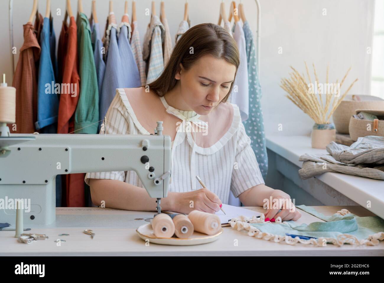 Stilista di moda disegno vestiti schizzo whie seduta al suo posto di lavoro con macchina da cucire Foto Stock