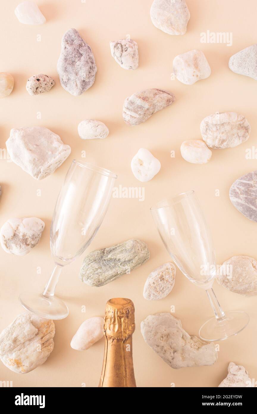 Una bottiglia di champagne e due bicchieri di champagne circondati da pietre dal mare su sfondo crema. Colori monocromatici. Una dolce estate romanti Foto Stock