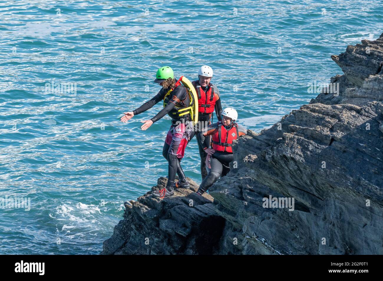 Una guida di coastering che consiglia ai vacanzieri come saltare in sicurezza dalle rocce su Towan Head a Newquay in Cornovaglia. Foto Stock