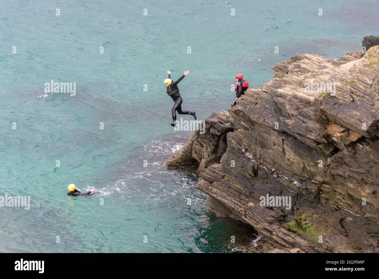 Un turista che salta dalle rocce durante una sessione di coastering intorno alla zona intercorrente a Towan Head a Newquay in Cornovaglia. Foto Stock