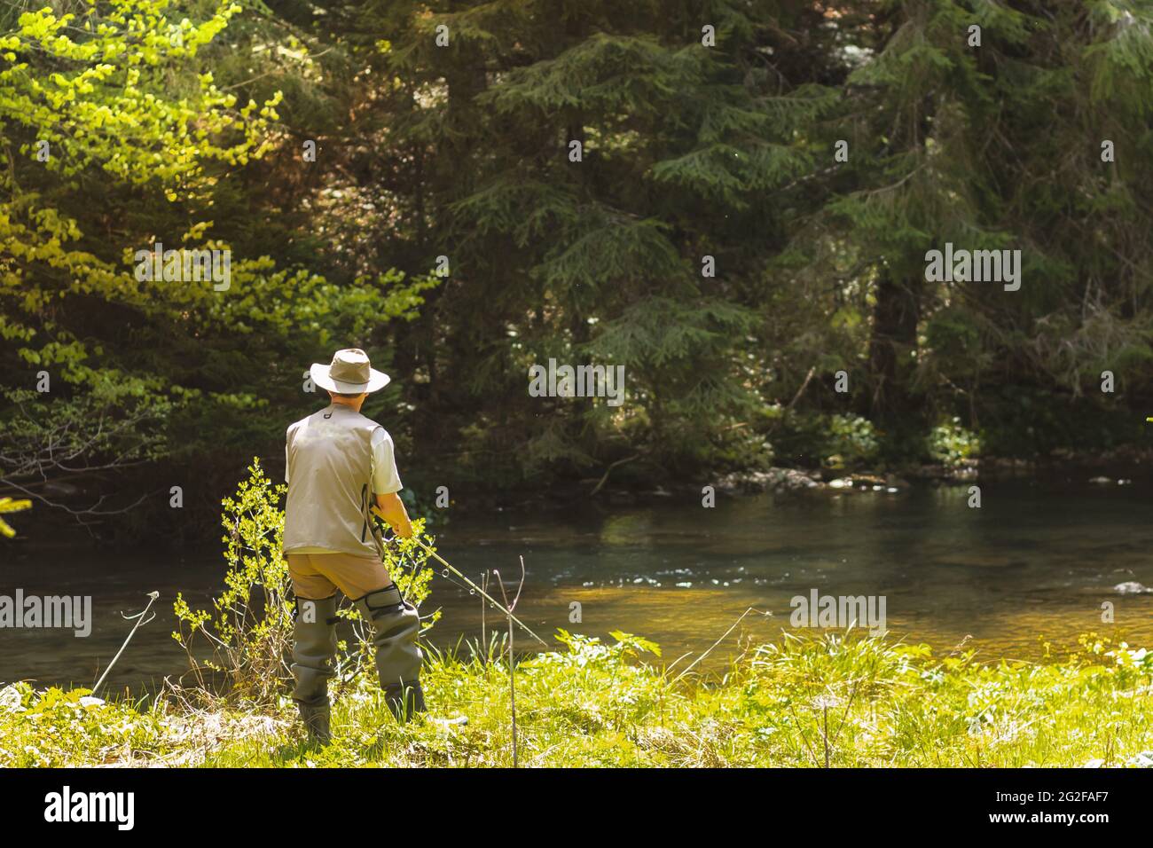 Vista posteriore di un uomo in abiti speciali pesca su una riva del lago Foto Stock