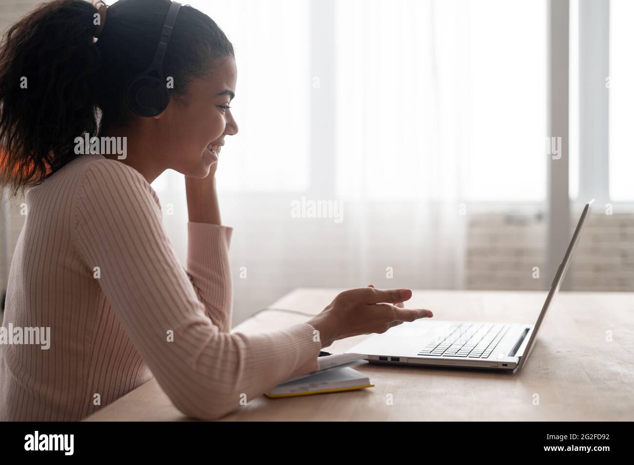 Vista laterale una giovane donna multirazziale che indossa una cuffia che tiene una riunione video, parla con colleghi o amici tramite connessione video, una studentessa che impara a distanza. Concetto di videochiamata Foto Stock