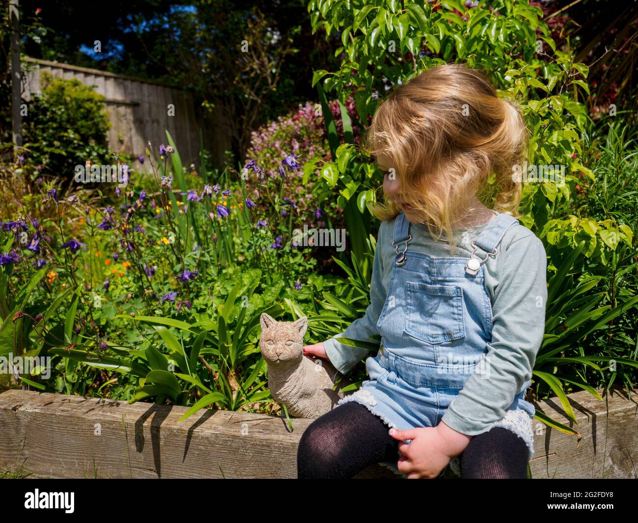 Bambino piccolo che stropicca un gatto ornamento giardino, Devon, UK Foto Stock