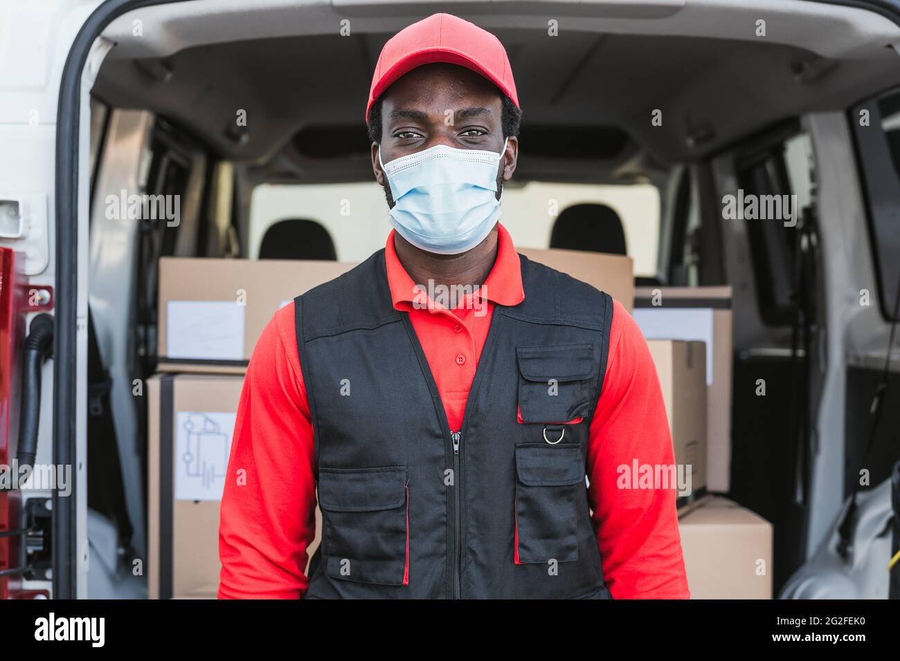Uomo di consegna africano che lavora mentre indossa la maschera facciale per evitare diffusione del virus corona - persone che lavorano con consegna rapida durante focolaio del virus corona Foto Stock