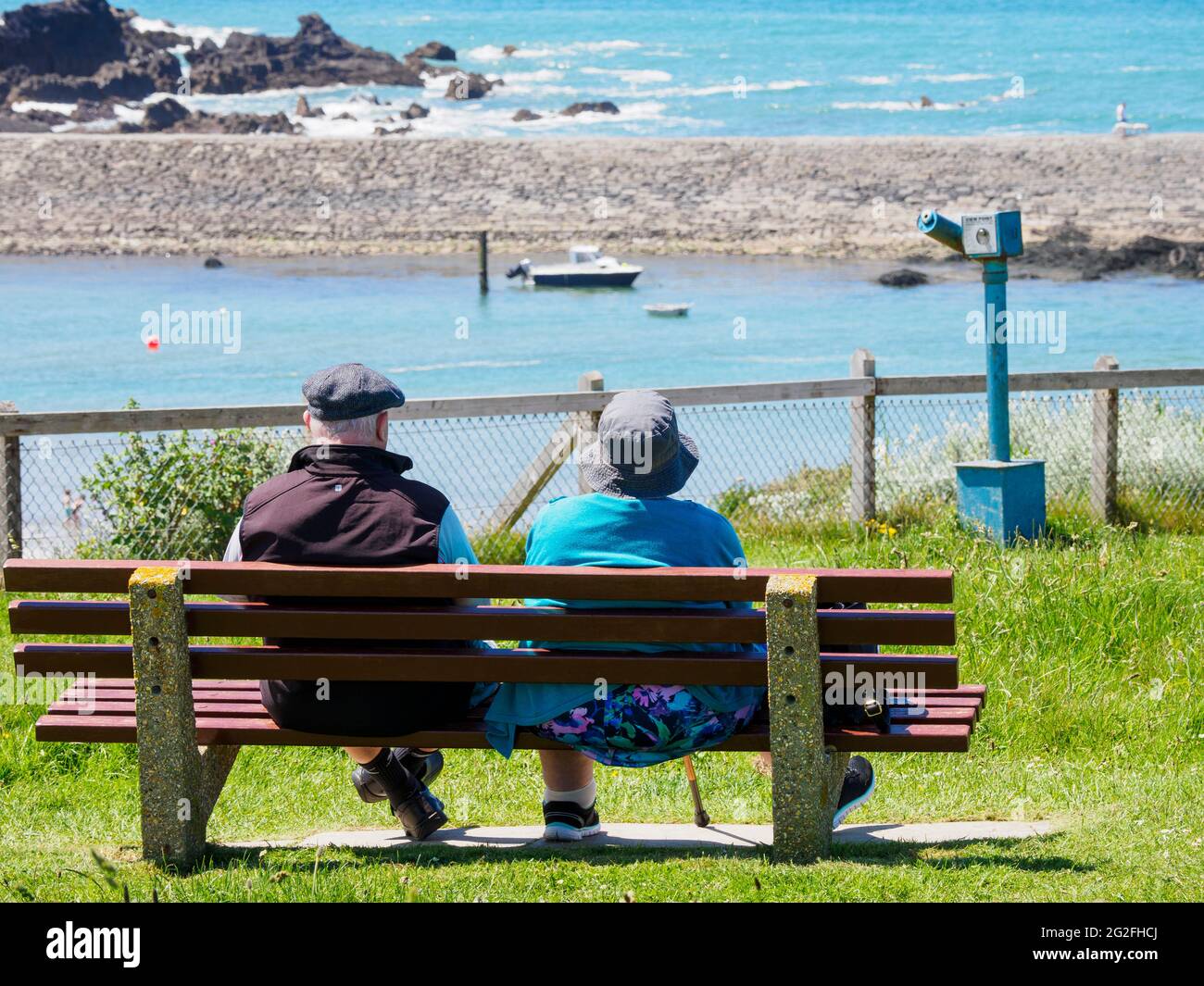 L'uomo anziano e la donna si sedettero su una panchina pubblica che guardava verso il mare, Bude, Cornovaglia, Regno Unito Foto Stock