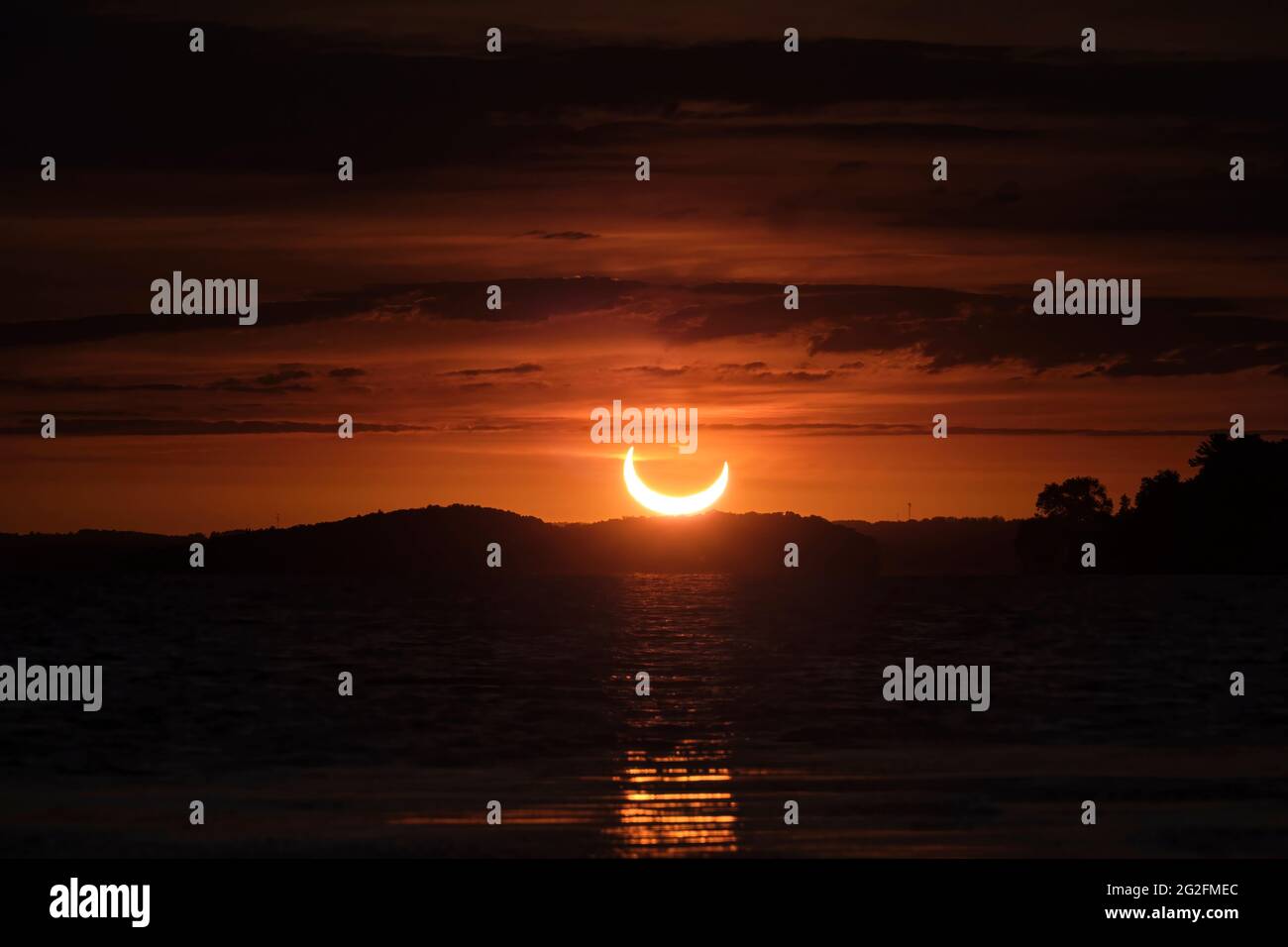 Tra strati di nuvole, una parziale eclissi solare è visto all'alba sul lago di riso, Ontario, come il sole, parzialmente coperto dalla luna, sorge in un essere Foto Stock