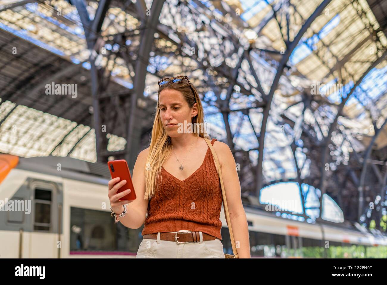 Giovane donna in attesa alla piattaforma della stazione ferroviaria utilizzando lo smartphone Foto Stock