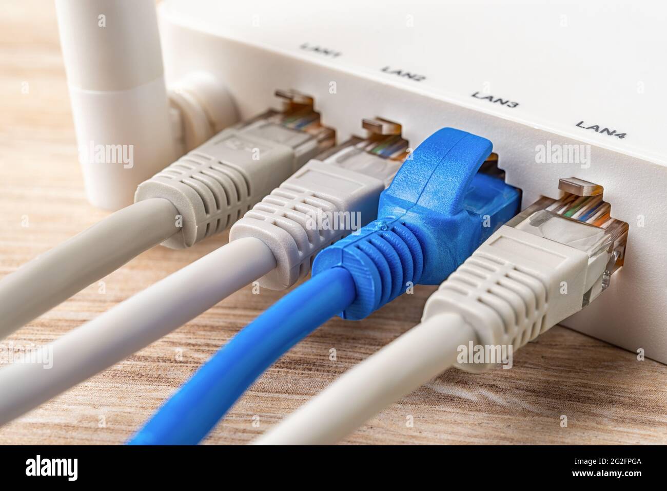 Quattro cavi di rete collegati al router wireless Wi-Fi bianco su una scrivania in legno. Il router wlan macro di casa e ufficio fornisce la connessione a Internet. Foto Stock