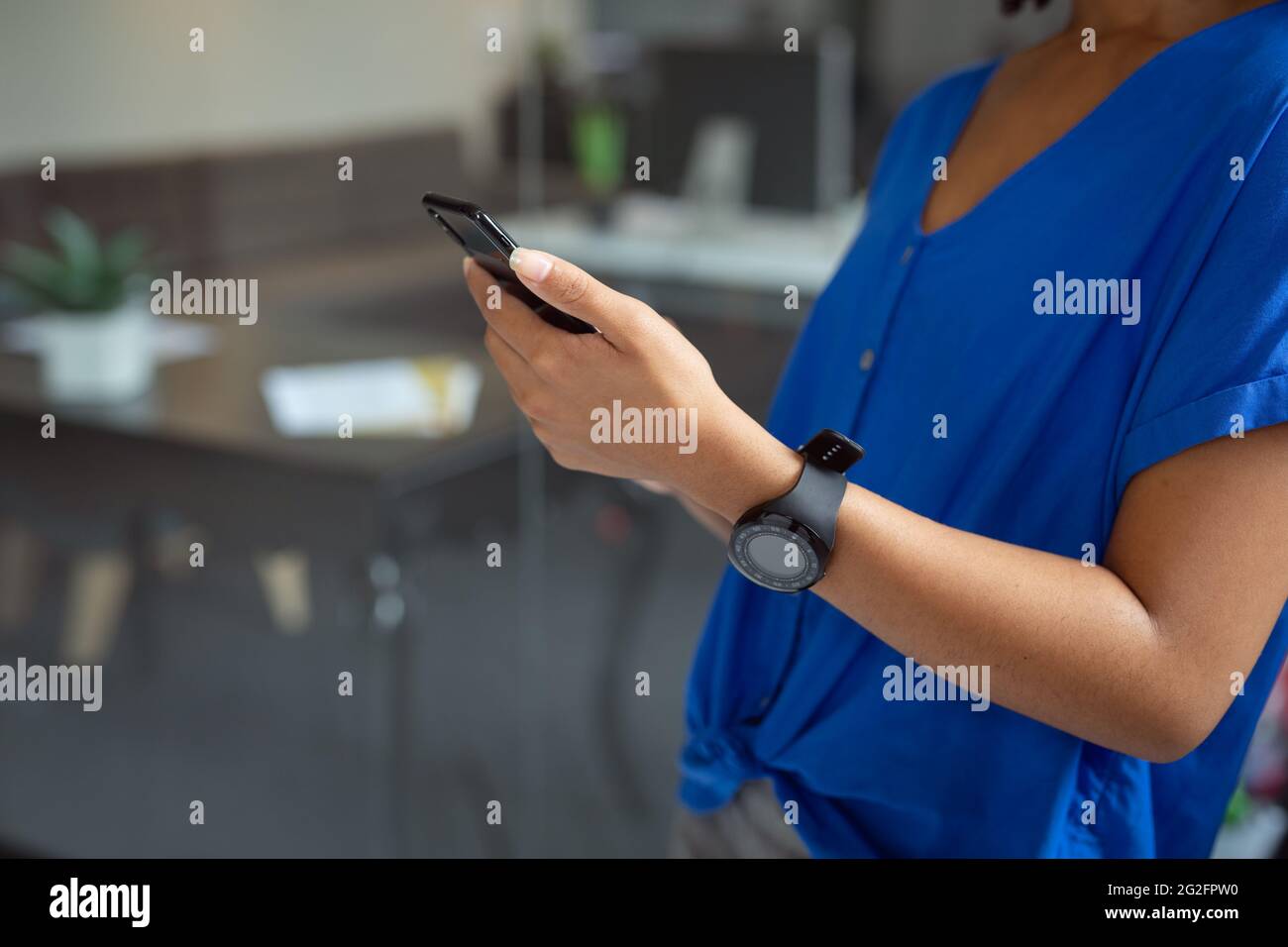 La sezione centrale della donna d'affari afroamericana che usa lo smartphone in piedi in ufficio Foto Stock