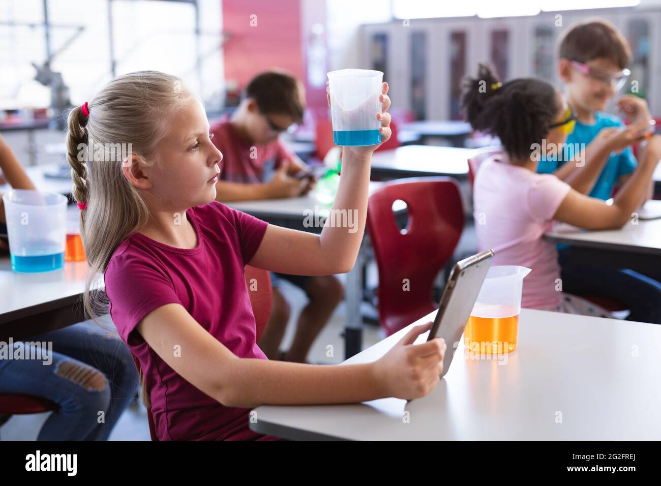 Ragazzo caucasico che tiene un bicchiere e una tavoletta digitale in classe scientifica in laboratorio Foto Stock