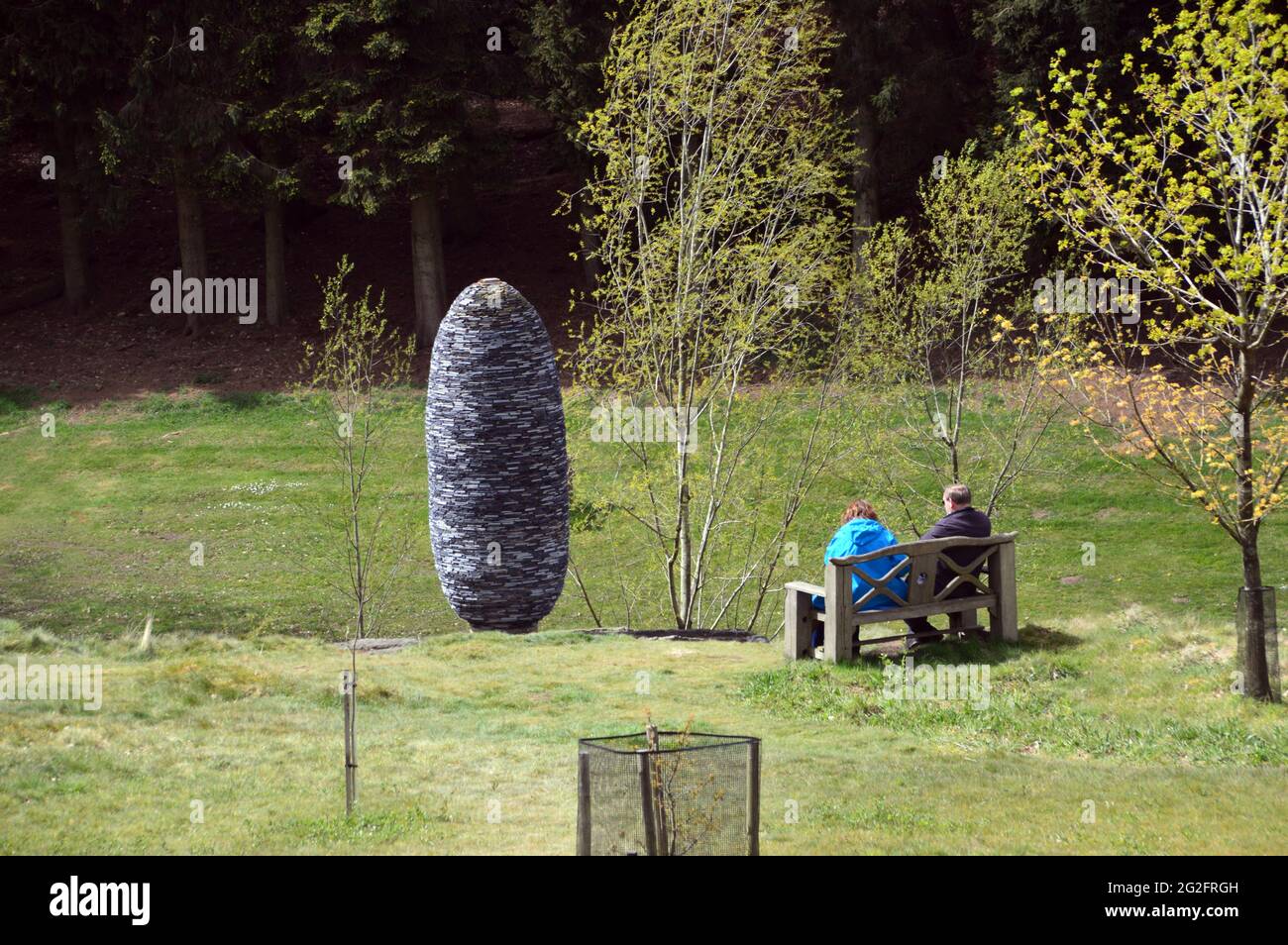 Coppia seduta sul banco di legno che ammira la scultura di pietra 'Fir Cone', il Giardino Himalayano e il Parco delle sculture, Grewelthorpe, Ripon, North Yorkshire. Foto Stock