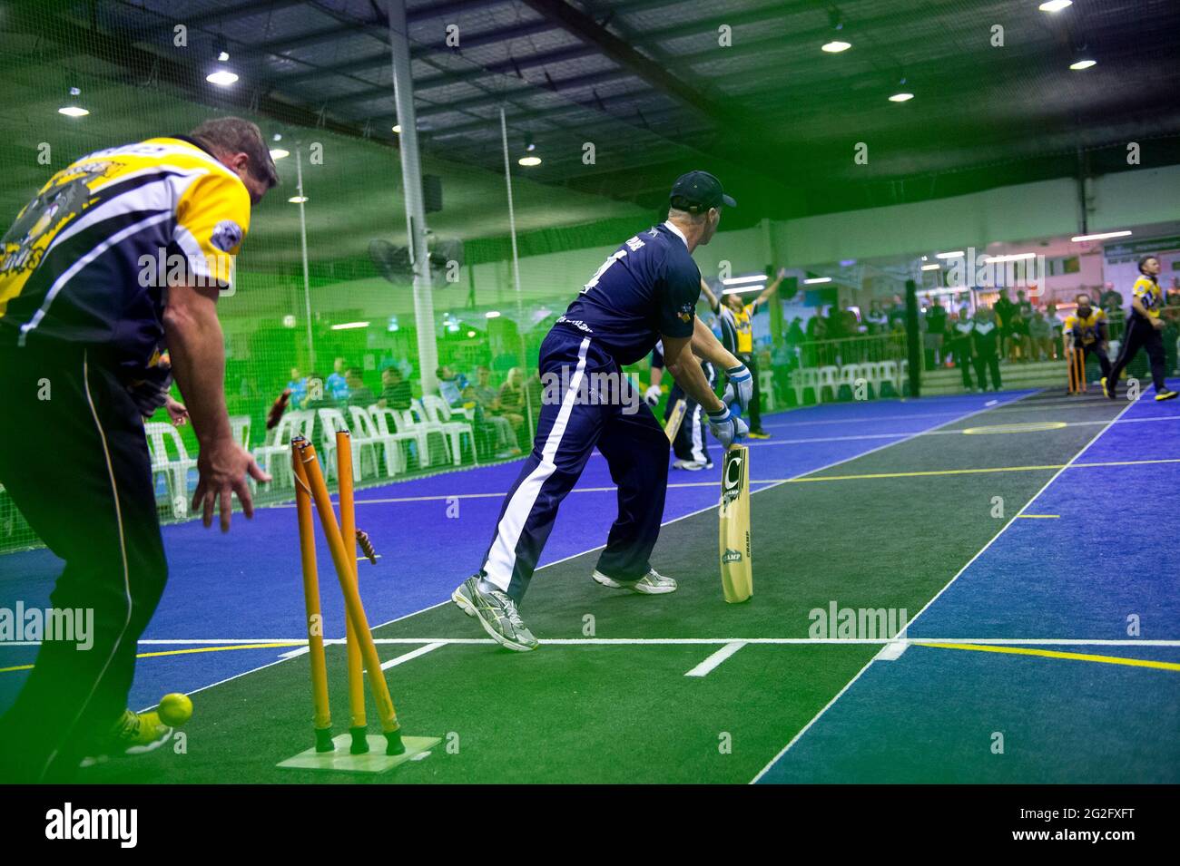 Le parate e le chiocciole volano mentre un battitore è fuori piegato in una partita di Cricket indoor Foto Stock