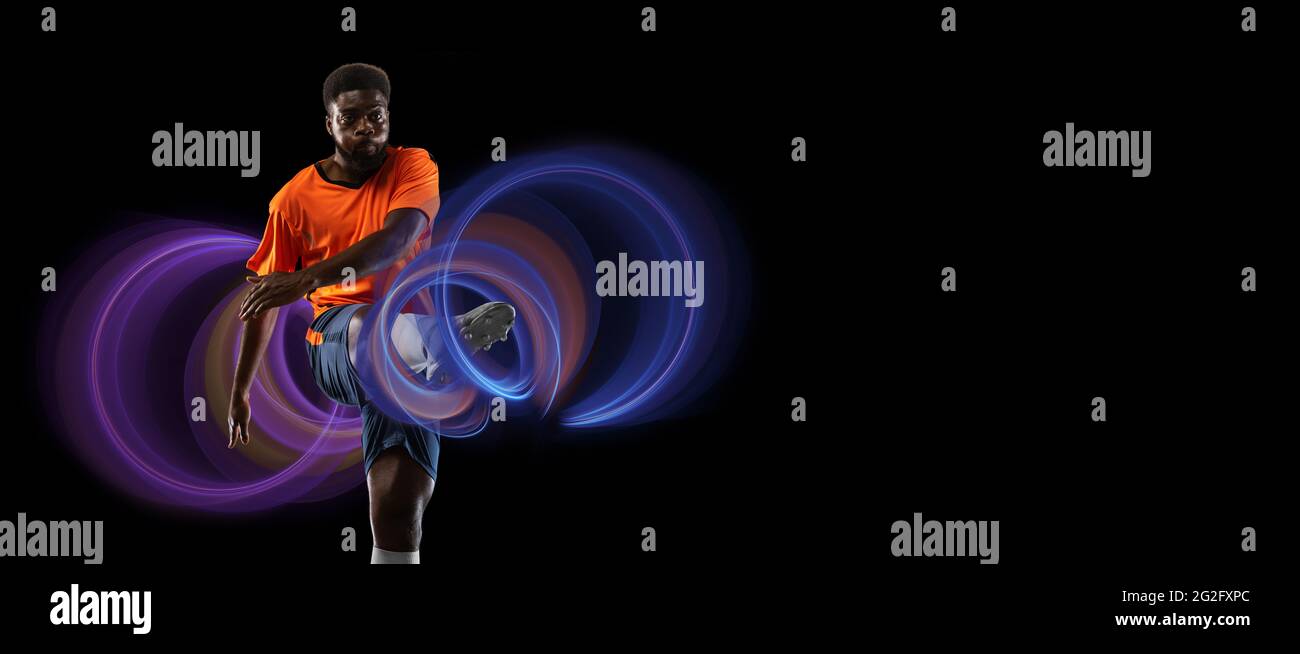 Giovane calcio africano, calciatore di calcio in luce al neon su sfondo nero. Concetto di movimento e azione nello sport. Allenamento in salto, volo. Sport Foto Stock