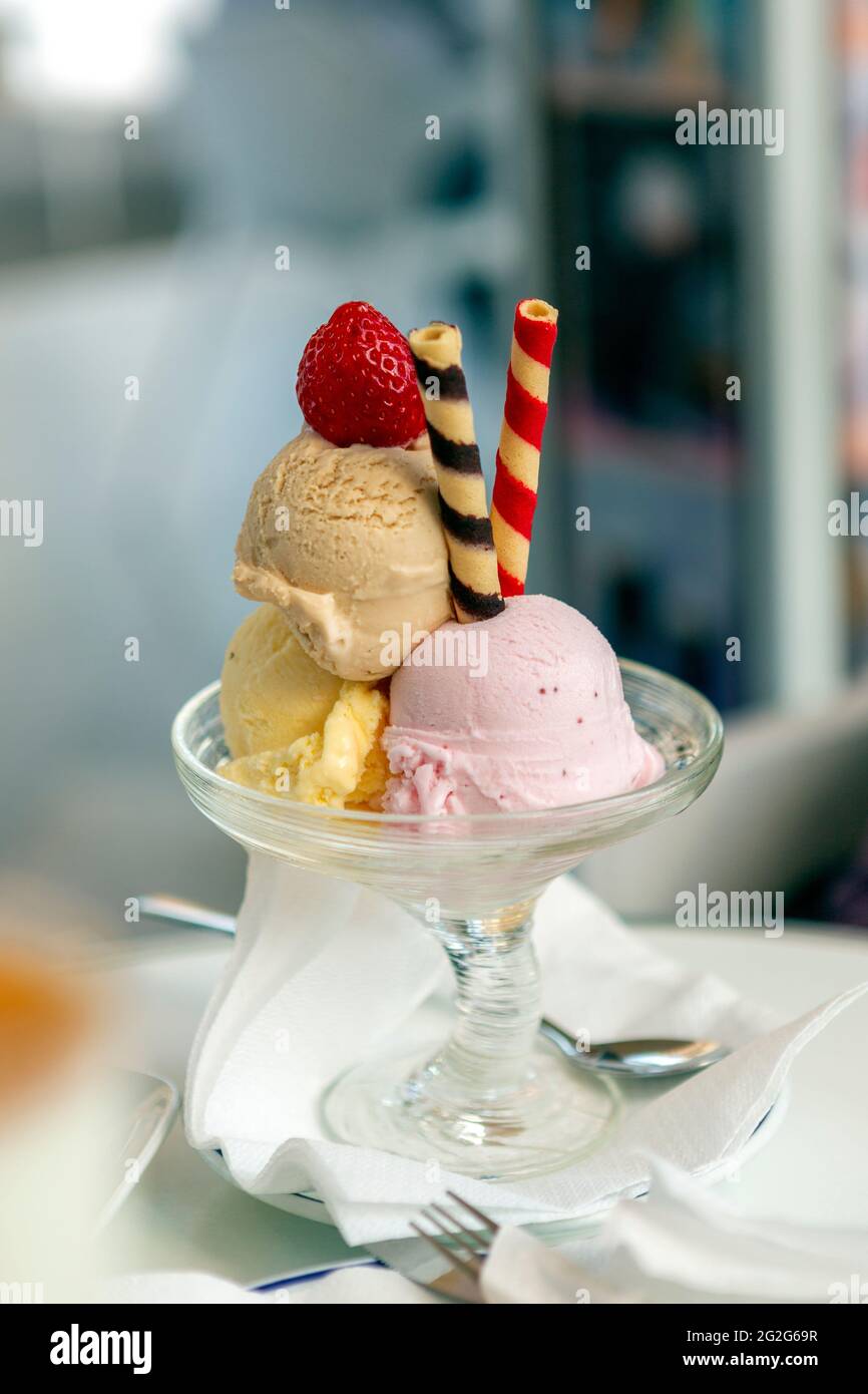 Gelato al gelato con tre gusti, accompagnato da wafer colorati a spirale, il tutto presentato in una bella tazza di vetro, sormontata con una fragola sulla parte superiore. Foto Stock