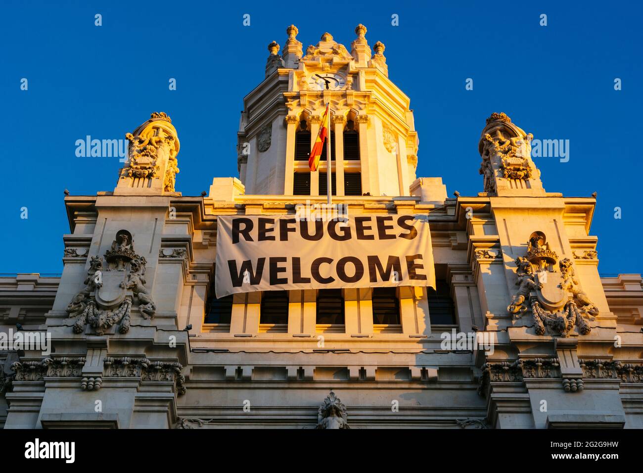 Torre centrale con bandiera 'i rifugiati sono benvenuti'. Palazzo Cibeles - Palacio de Cibeles è un complesso composto da due edifici con facciate bianche ed è loc Foto Stock