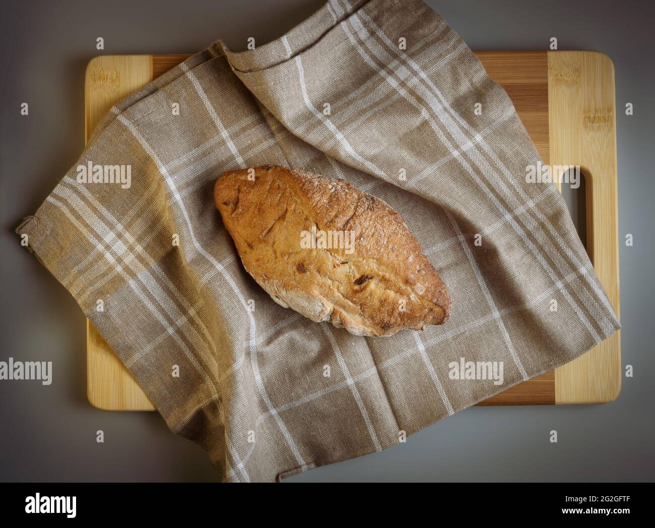 Pane di campagna caldo appena sfornato con farina, appena sfornato su un asciugamano di lino marrone con quadrati bianchi, un pannello di legno. Fotographia appetitosa. Foto Stock