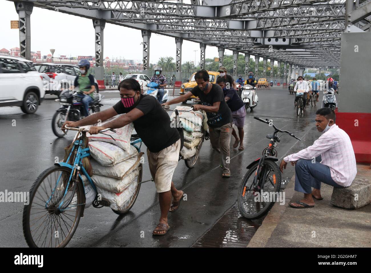 Kolkata, India. 11 Giugno 2021. I pendolari si occupano delle merci e delle loro biciclette oltre il caratteristico ponte Howrah sul fiume Ganga. Regolarmente l'aumento del prezzo del carburante in India. Il prezzo della benzina e del diesel oggi ha fatto un'ora di ventitreesima volta in meno di sei settimane, il prezzo della benzina oggi attraversa RS 102/litro nella città di Mumbai. (Foto di Dipa Chakraborty/Pacific Press) Credit: Pacific Press Media Production Corp./Alamy Live News Foto Stock